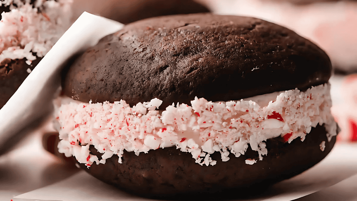 A close-up of a chocolate whoopie pie with a peppermint filling. The filling is speckled with crushed peppermint candies, adding a festive touch. The background shows more of these desserts.