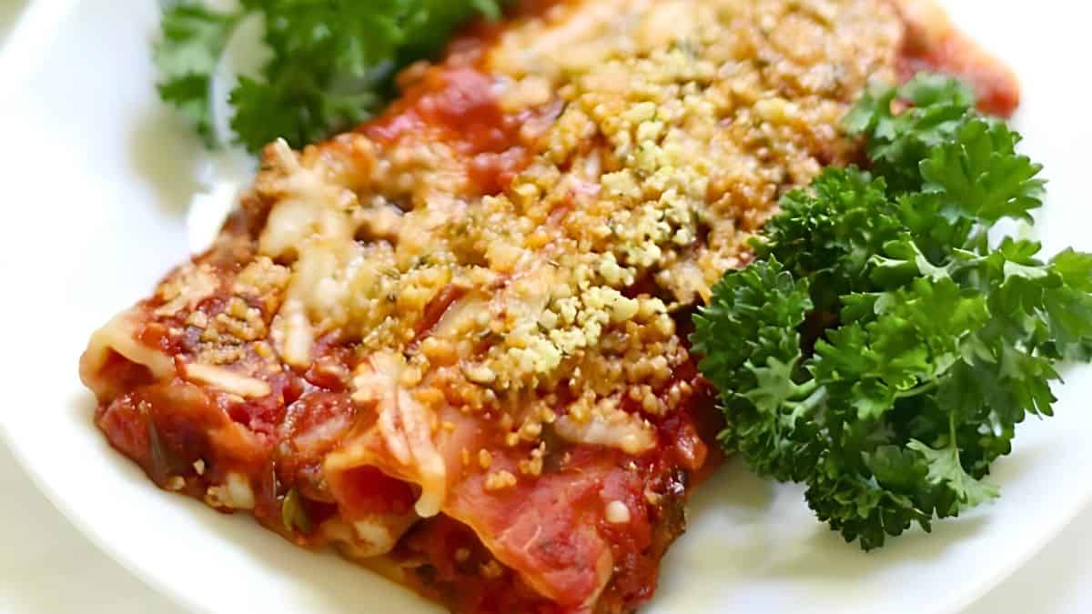 A plate of stuffed pasta rolls topped with tomato sauce and grated cheese. The pasta is garnished with fresh parsley, adding a pop of green to the dish.