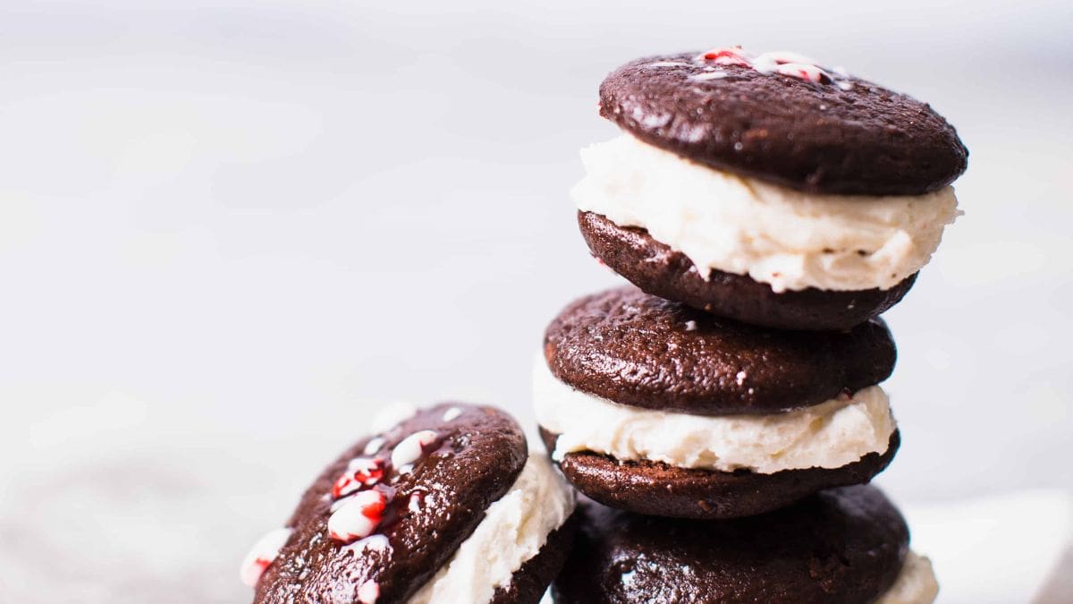 A stack of chocolate sandwich cookies with cream filling and crushed peppermint on top. The background is softly blurred.