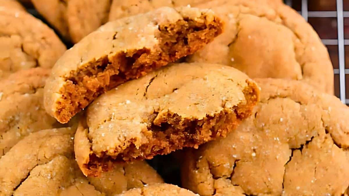 Close-up of freshly baked peanut butter cookies. One cookie is broken in half, showing its soft interior. The cookies are golden brown with a slightly cracked surface, resting on a cooling rack.