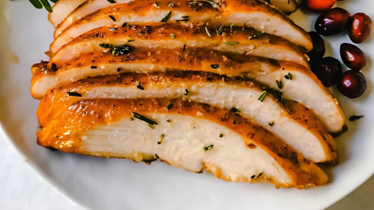 Sliced roasted turkey breast seasoned with herbs on a white plate, garnished with cranberries.