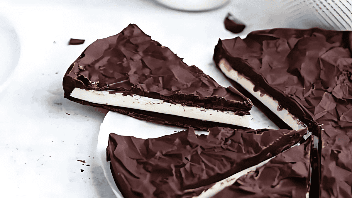 A sliced chocolate torte with a dark, crinkled chocolate top and a creamy white filling, arranged on a white surface. Some slices are removed, revealing the layered interior.