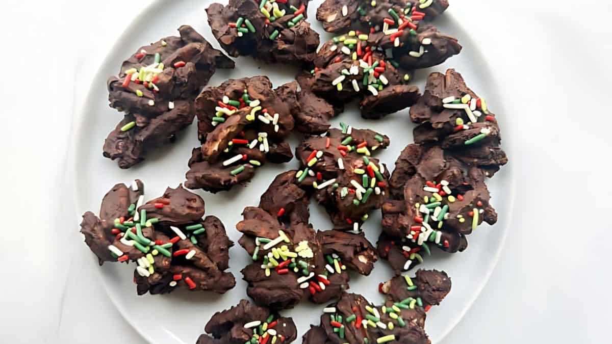 A white plate filled with chocolate clusters topped with colorful sprinkles, arranged randomly on the surface.