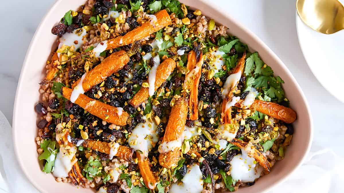 A triangular dish filled with a colorful salad. It includes roasted carrots, black beans, fresh cilantro, and dollops of yogurt. The salad is topped with chopped pistachios, giving it a vibrant and appetizing appearance.