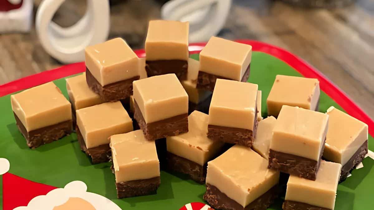 A stack of peanut butter chocolate fudge squares on a festive green tray with red and white decorations. The fudge has a light brown peanut butter layer on top of a darker chocolate base.