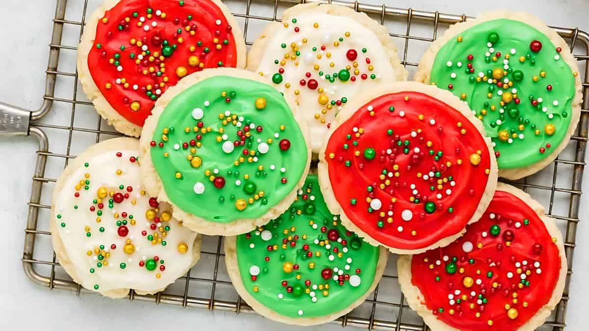 A cooling rack holds sugar cookies with red, green, and white icing. The cookies are decorated with colorful sprinkles in red, green, yellow, and white.