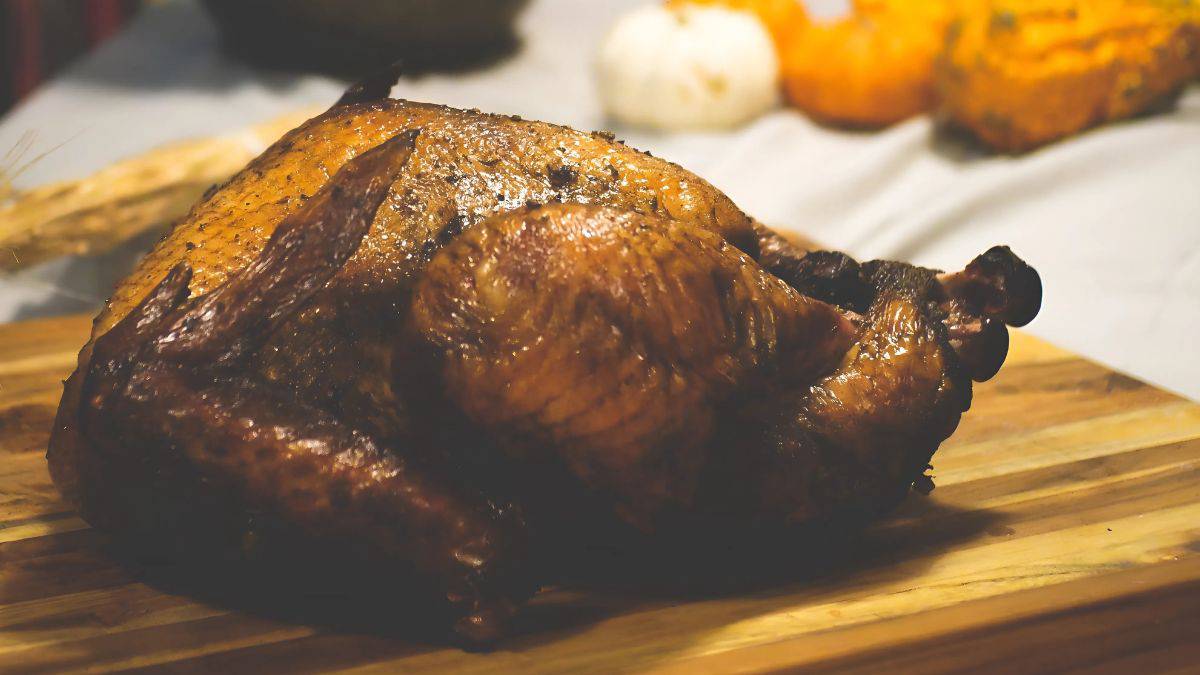 A roasted turkey on a wooden board in soft lighting, surrounded by blurred white and orange pumpkins in the background.