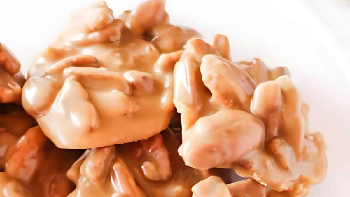 Close-up of a pile of pralines with a glossy caramel coating, displaying the texture of nuts embedded in the candy. The pralines are arranged on a white surface, highlighting their rich, brown color and shiny finish.