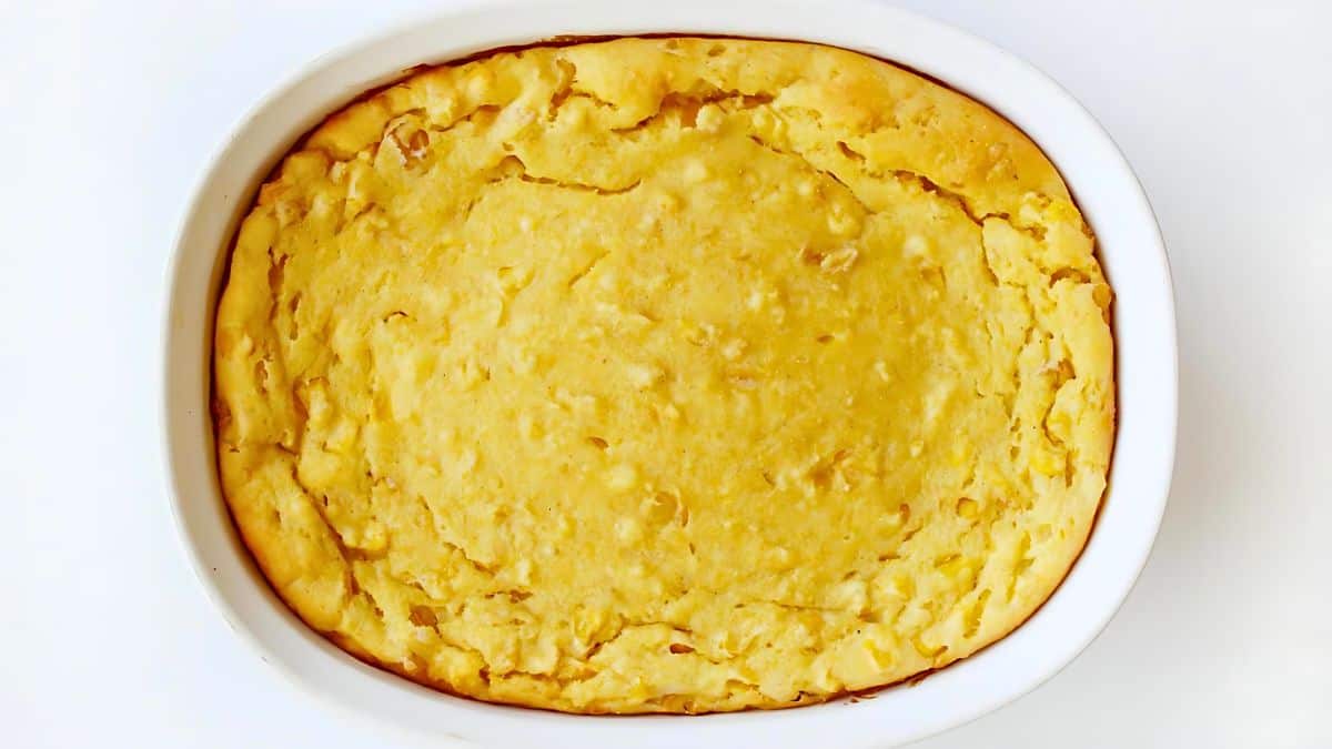 A baked casserole in a white oval dish, featuring a golden-brown crust on top. The surface is slightly uneven and has a light, fluffy texture. The edges are slightly browned, indicating it is freshly baked.