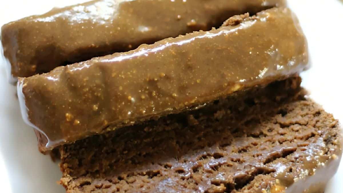 Close-up of chocolate fudge bars atop slices of chocolate bread on a white plate. The fudge bars have a glossy texture, highlighting the rich chocolate coating. The bread below appears soft and moist, complementing the dessert.