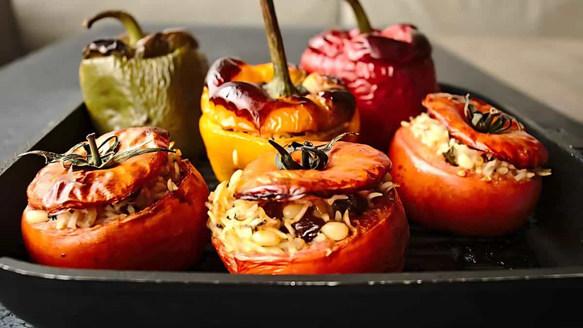 A tray of roasted stuffed vegetables, including tomatoes and bell peppers, filled with rice and pine nuts. The vegetables are arranged neatly, showcasing a vibrant mix of red, yellow, and green colors.