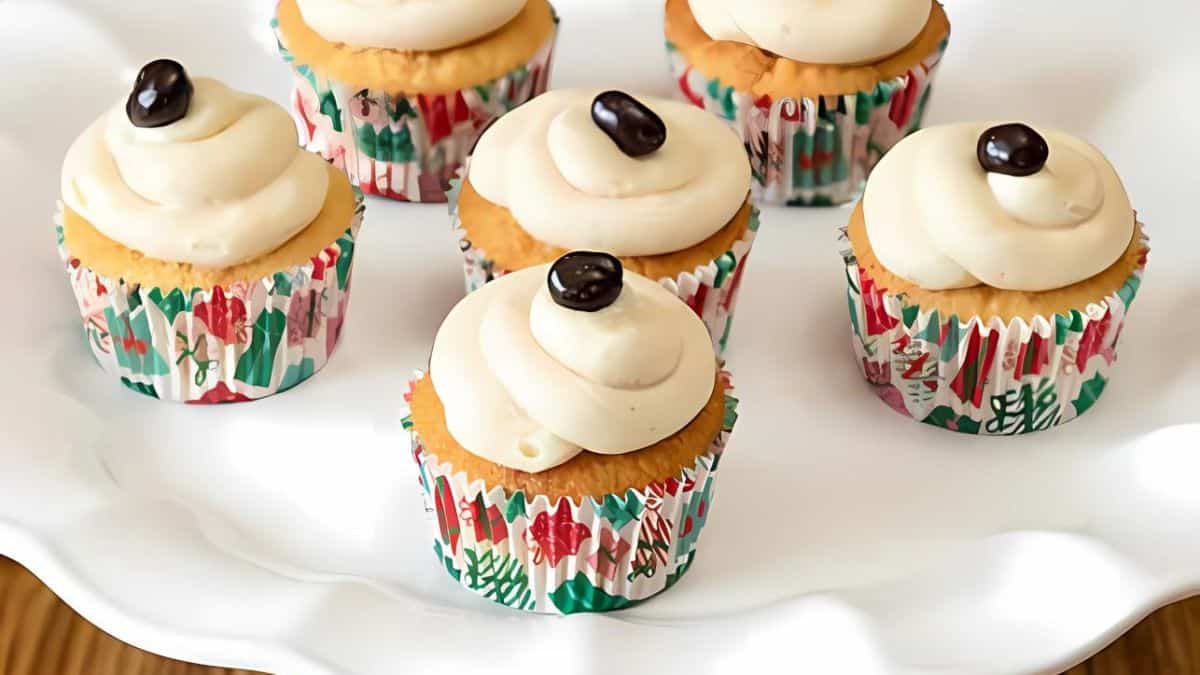 Cupcakes with creamy frosting and single coffee bean toppings, displayed on a white plate. They are wrapped in festive, colorful cupcake liners.