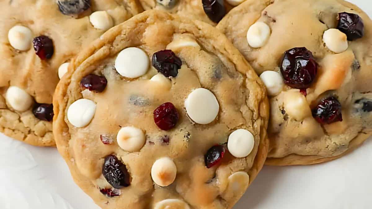 Close-up of cookies with white chocolate chips and dried cranberries on a white surface.
