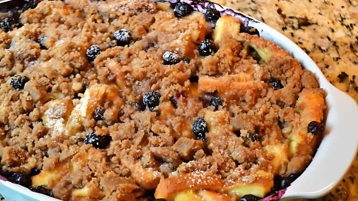 A freshly baked casserole dish filled with a blueberry and crumble-topped dessert sits on a countertop. The crumbly topping is golden brown with visible blueberries scattered throughout, giving it a delicious homemade appearance.