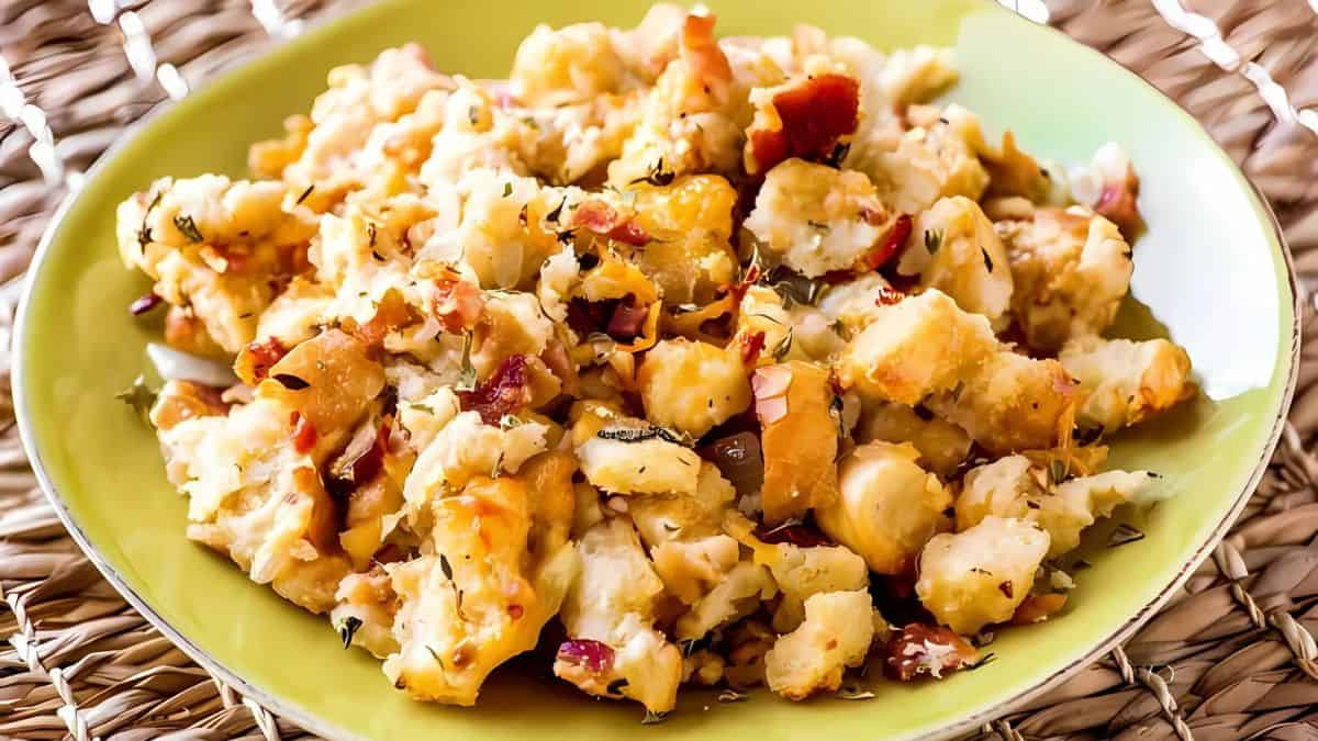 A plate of scrambled eggs with diced bacon and herbs, served on a green dish on a woven placemat.