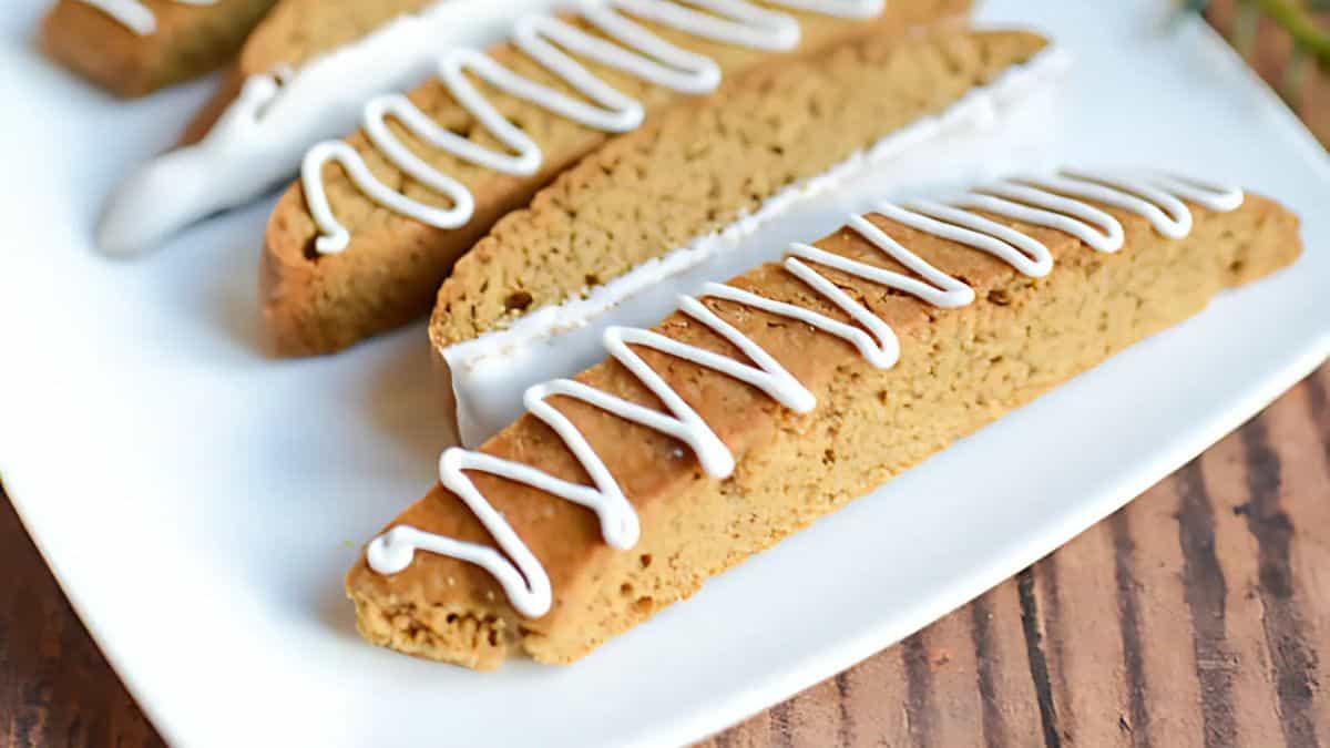 A close-up of several biscotti on a white plate, decorated with white icing in zigzag patterns. The biscotti are light brown and neatly arranged, creating an inviting and delicious presentation.