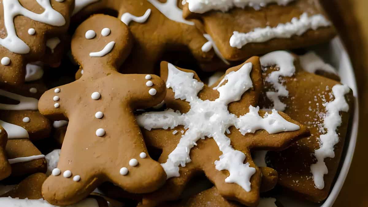 A close-up of gingerbread cookies decorated with white icing. The cookies are shaped like a smiling gingerbread person and a snowflake, among others, arranged on a plate.