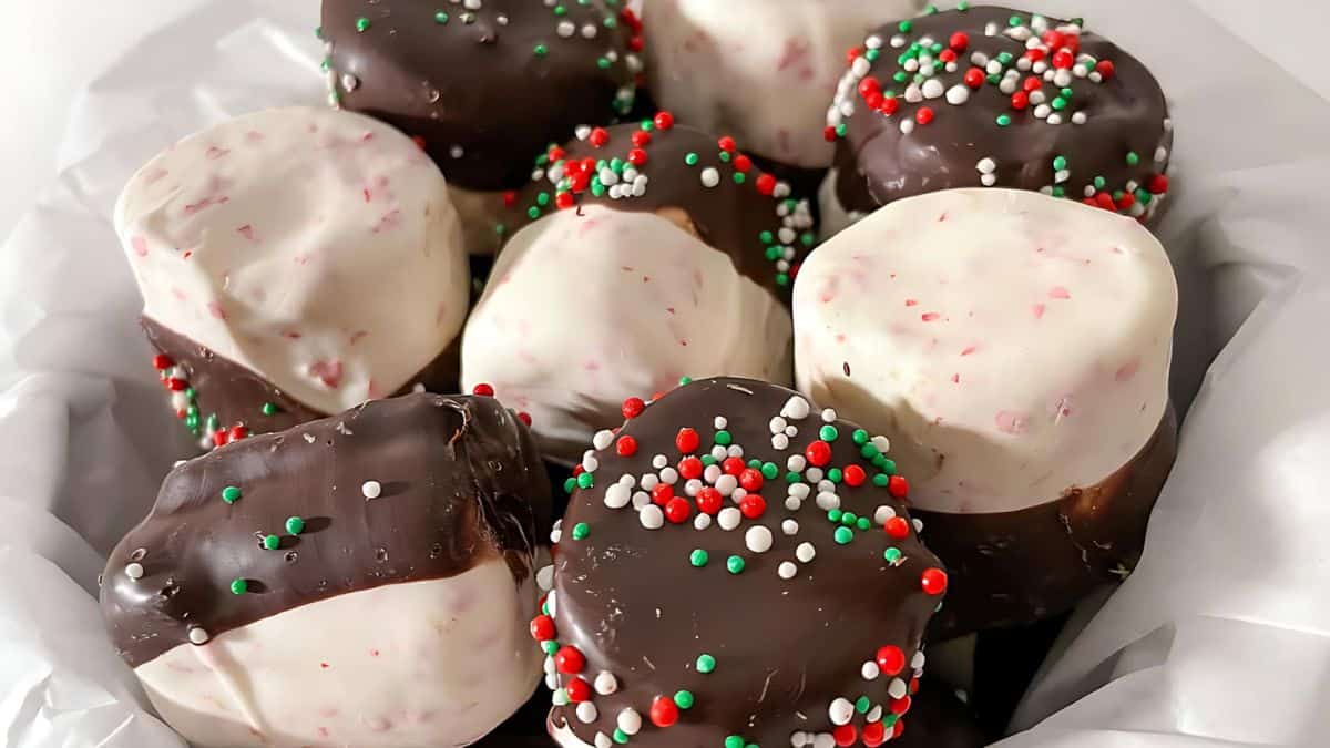A tray of round, chocolate-covered treats, some with white chocolate and others with dark, sprinkled with festive red, green, and white nonpareils, placed on white parchment paper.