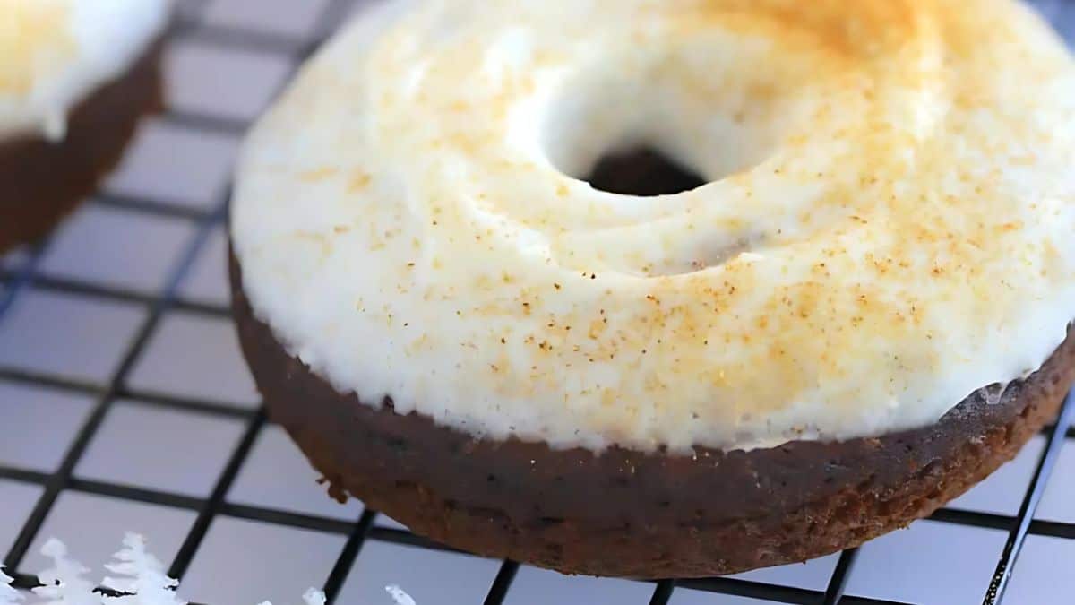 A chocolate donut with white icing and a sprinkle of orange zest sits on a cooling rack.