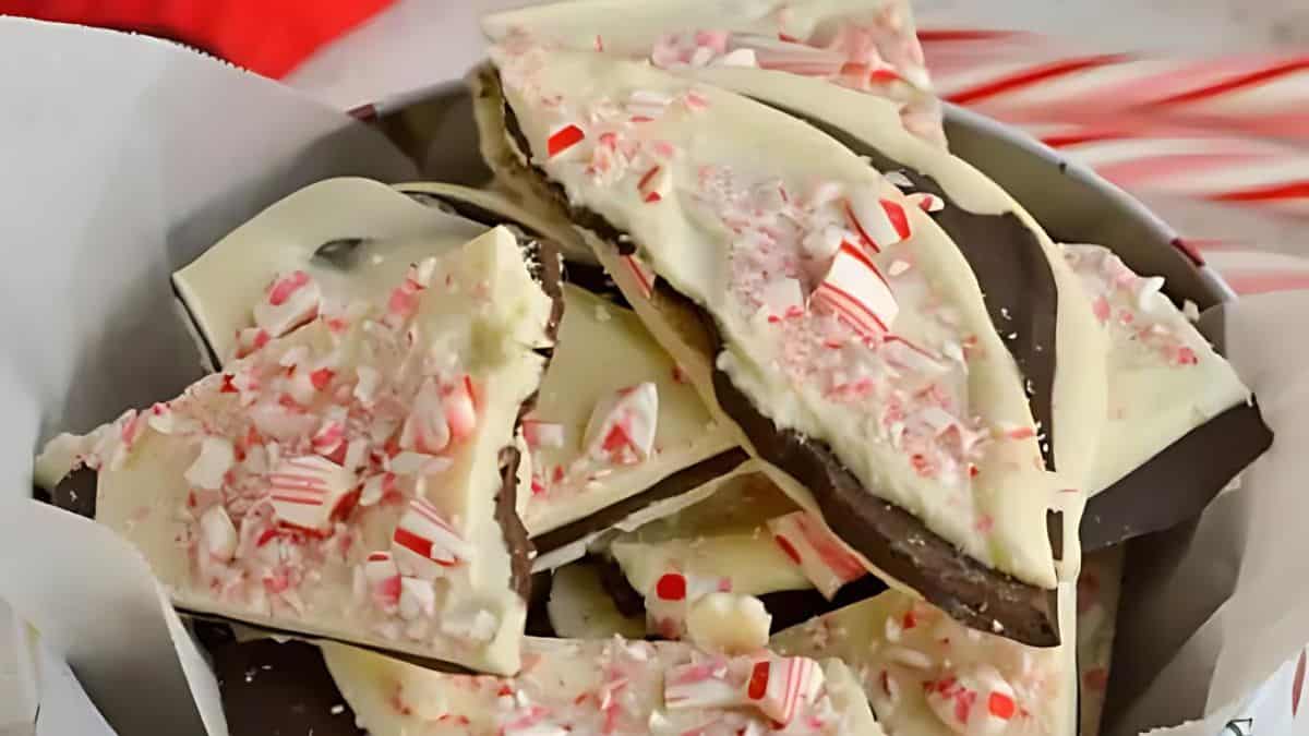 A bowl filled with pieces of peppermint bark, featuring layers of dark and white chocolate sprinkled with crushed candy canes. The peppermint bark is arranged on a sheet of white parchment paper.