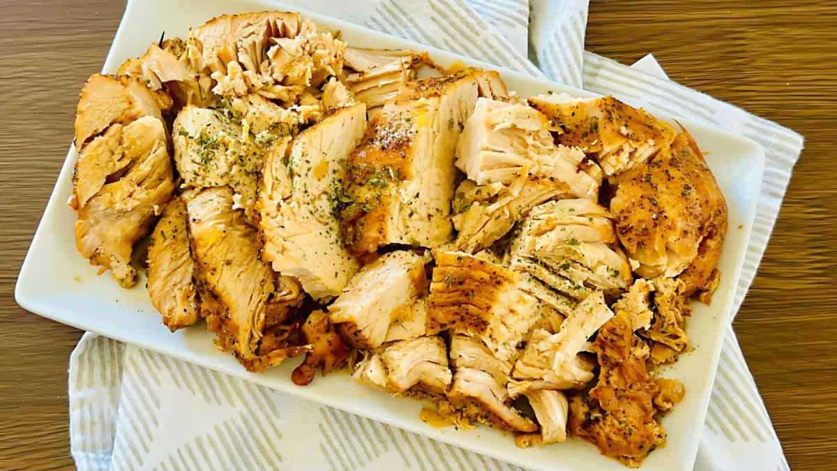 A rectangular white plate filled with sliced, seasoned baked salmon, garnished with herbs. The plate is resting on a striped cloth with a wooden table beneath.