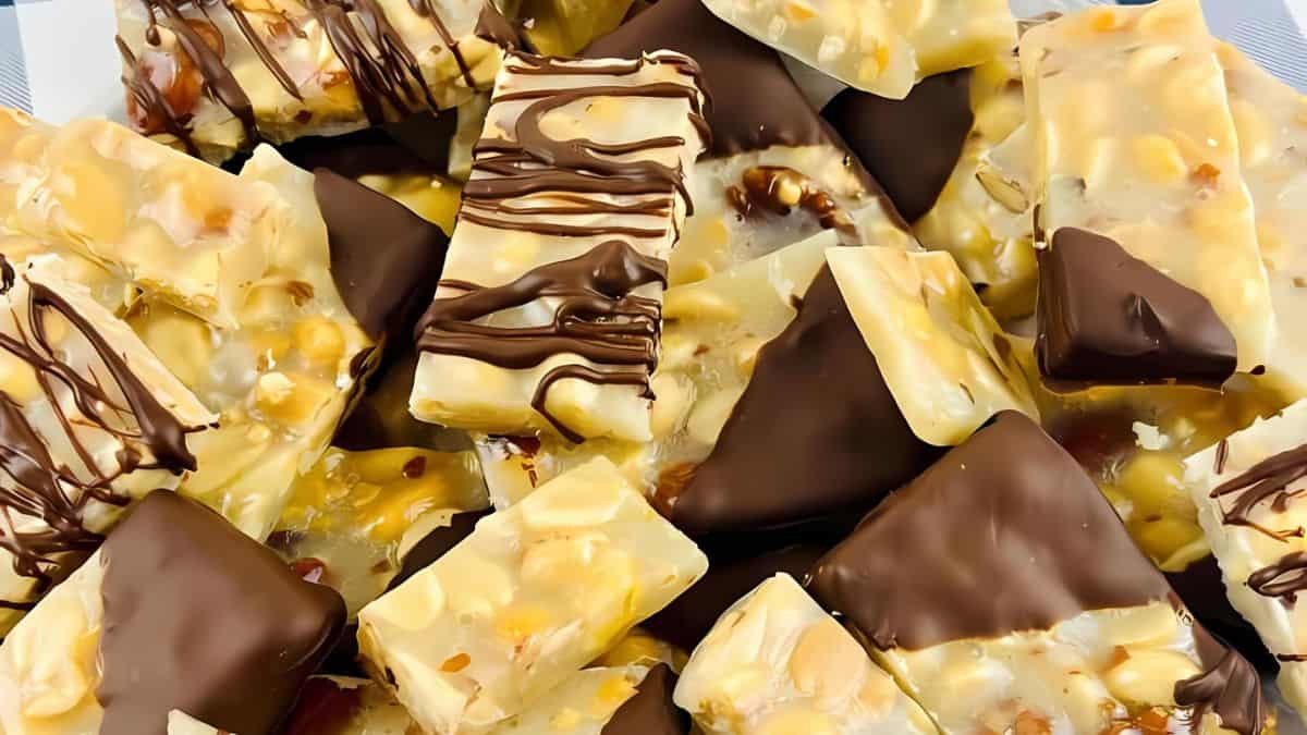 A pile of nut bars, some partially dipped in dark chocolate and others drizzled with chocolate. The bars contain visible nuts and a caramel-like coating, creating a tempting mix of sweet and nutty flavors.
