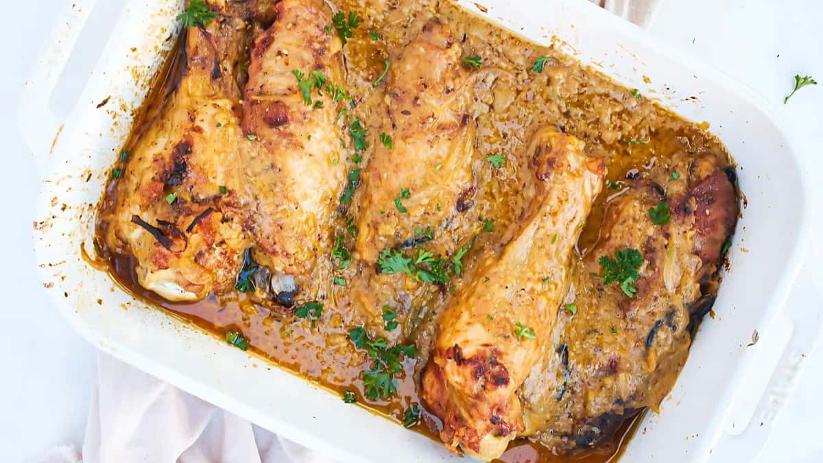 Baked chicken pieces in a white dish, topped with a golden-brown sauce and sprinkled with fresh parsley.