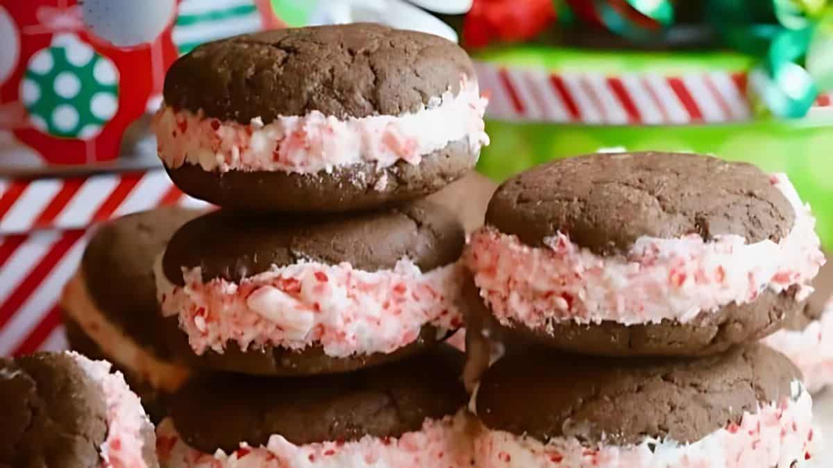 Chocolate sandwich cookies with creamy pink filling stacked in front of festive, colorful gift wrap and ribbons.