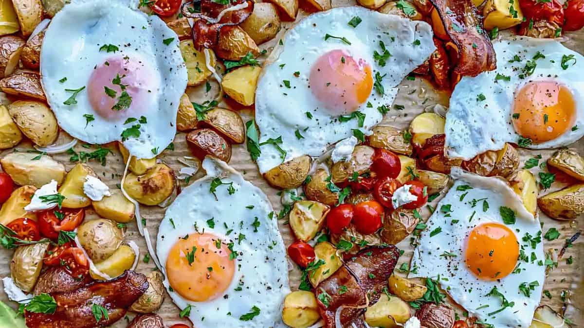 A sheet pan breakfast featuring sunny-side-up eggs, roasted potatoes, cherry tomatoes, and crispy bacon, garnished with fresh parsley. The ingredients are spread out evenly for a colorful and appetizing presentation.