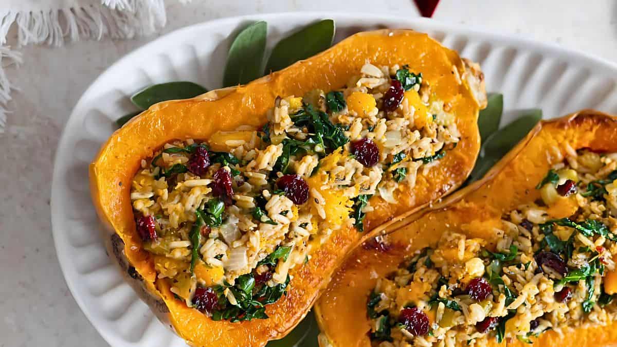 Stuffed butternut squash halves filled with a mixture of rice, spinach, cranberries, and herbs are displayed on a white oval platter. The vibrant colors and textures highlight a hearty, nutritious meal.