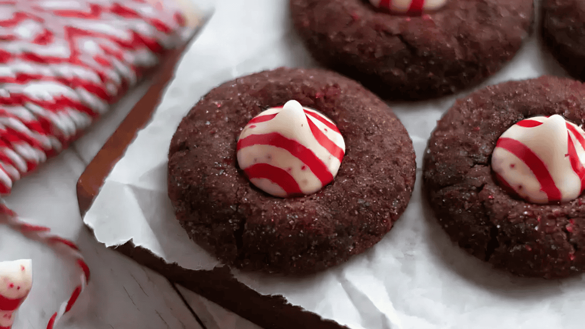 Close-up of chocolate cookies topped with red and white striped peppermint candies on a piece of parchment paper. A coil of red and white twine lies nearby, enhancing the festive presentation.