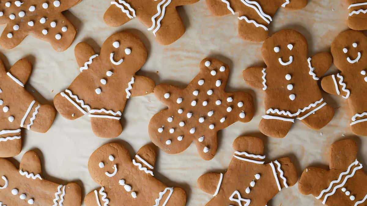 A collection of gingerbread cookies shaped like people, decorated with white icing for eyes, smiles, and clothing details, are arranged on a light surface. The cookies are all similarly designed, creating a festive and cheerful atmosphere.