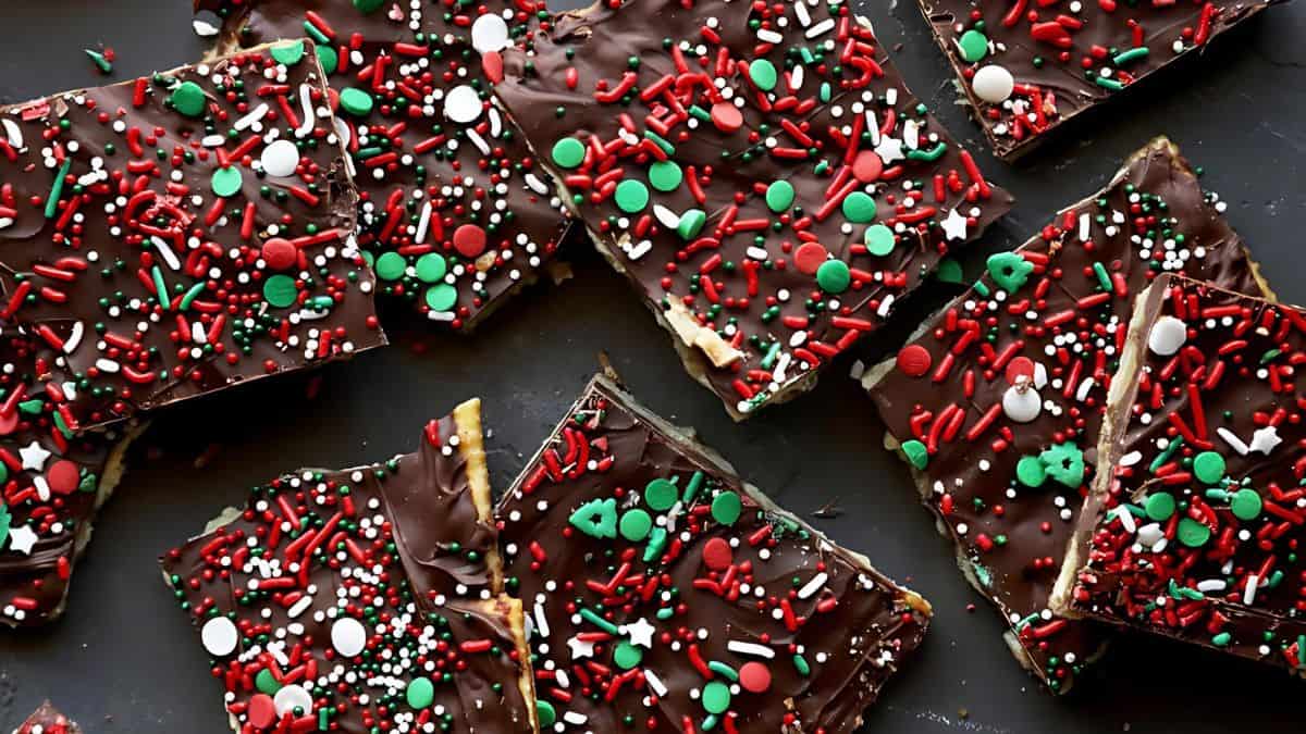 Festive chocolate bark pieces topped with red, green, and white sprinkles on a dark surface.