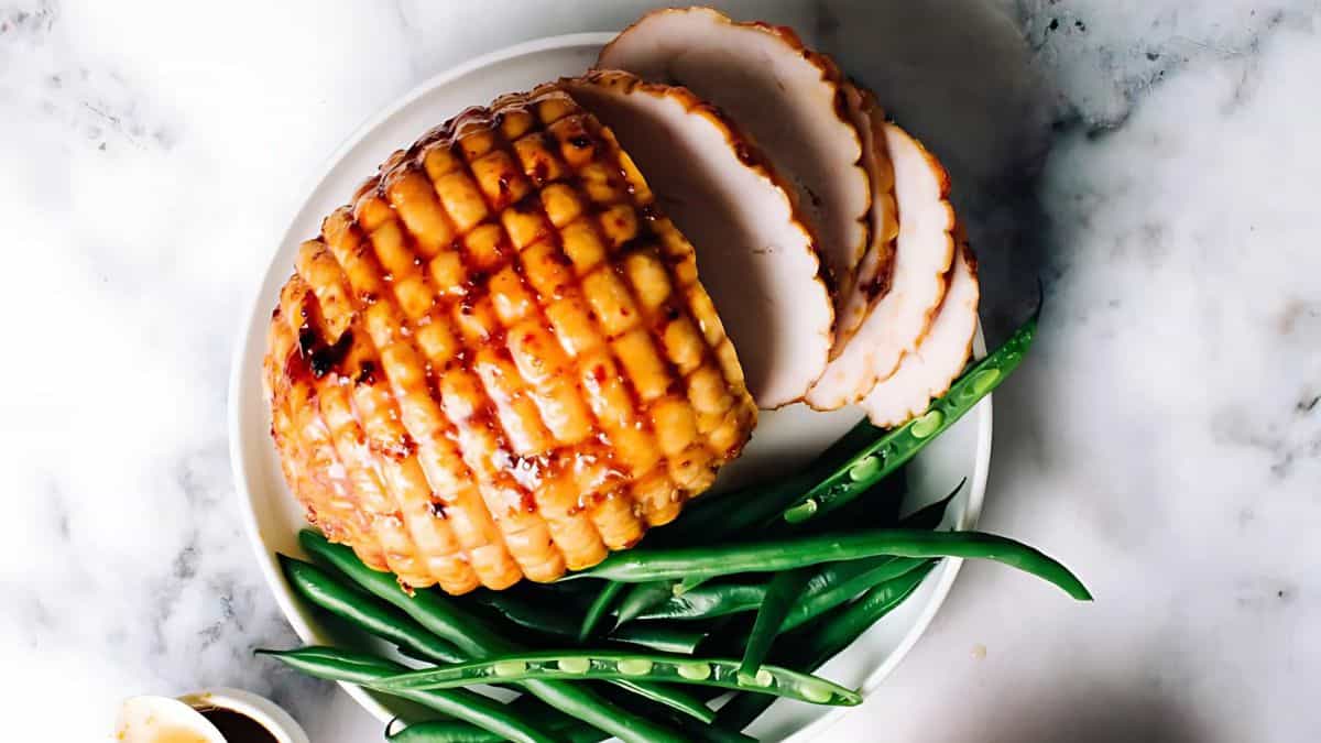 A glazed roasted turkey breast is sliced on a white plate, accompanied by fresh green beans. The marble surface underneath adds to the aesthetic, highlighting the dish's appetizing presentation.