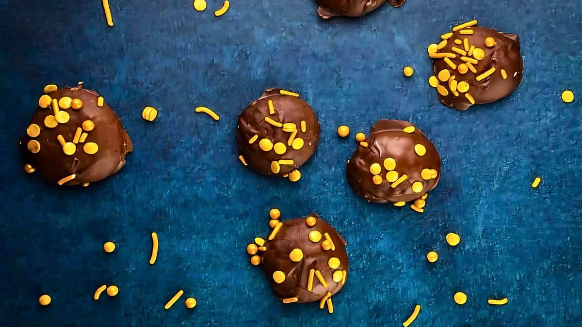 Chocolate-covered treats scattered on a blue surface, topped with yellow sprinkles and decorative circles. A few sprinkles are scattered around the treats.
