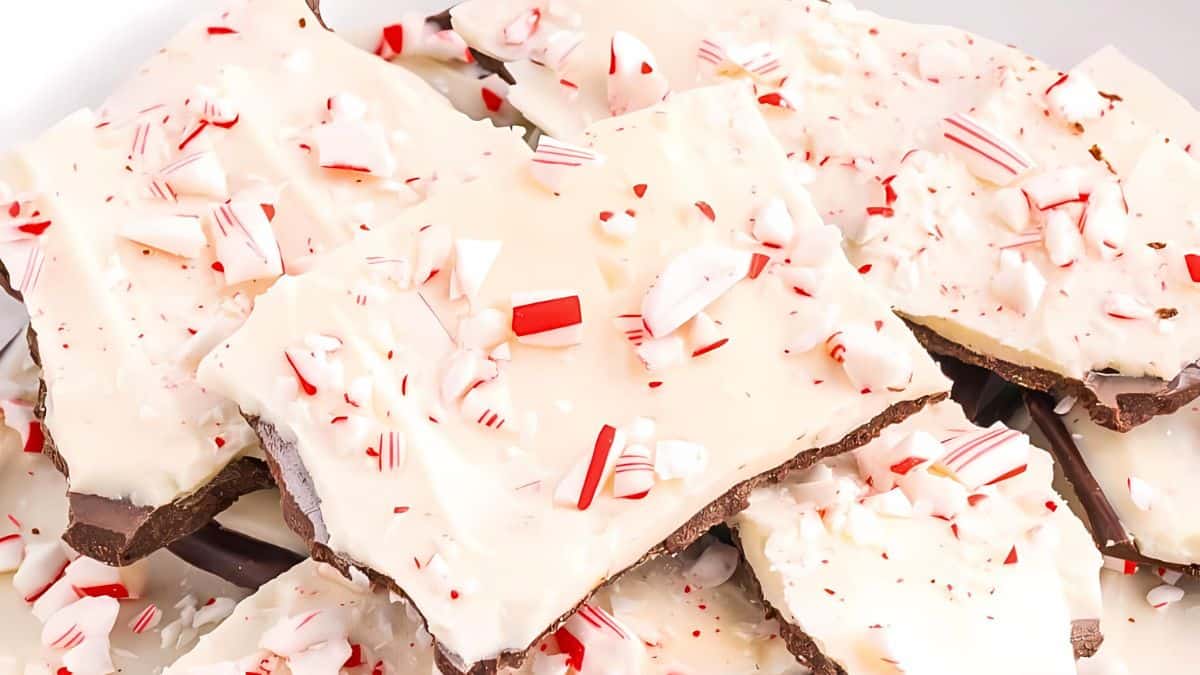 A pile of peppermint bark pieces, featuring layers of dark and white chocolate topped with crushed peppermint candy. The white chocolate surface is scattered with red and white candy bits, creating a festive appearance.