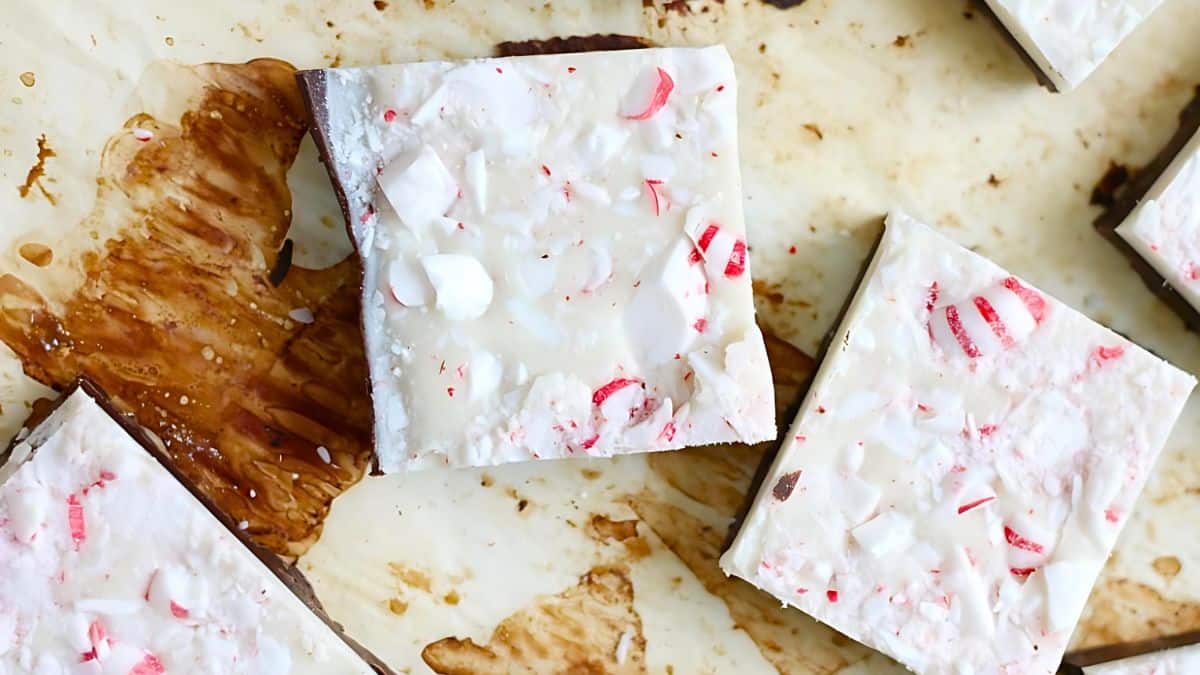 Top view of squares of white chocolate peppermint bark on a parchment paper. The bark is topped with crushed red and white peppermint candies, adding subtle color to the white chocolate surface.