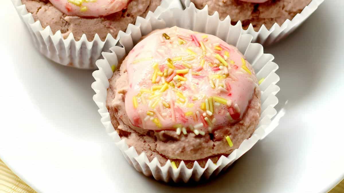 Close-up of chocolate cupcakes with pink frosting and colorful sprinkles, each cupcake in a white paper liner, arranged on a white plate.