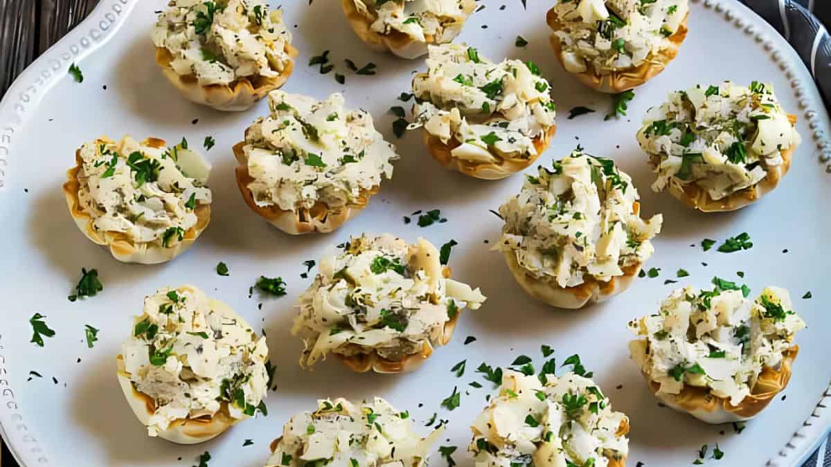 A white plate with multiple phyllo cups filled with creamy chicken and topped with herbs, garnished with chopped parsley.