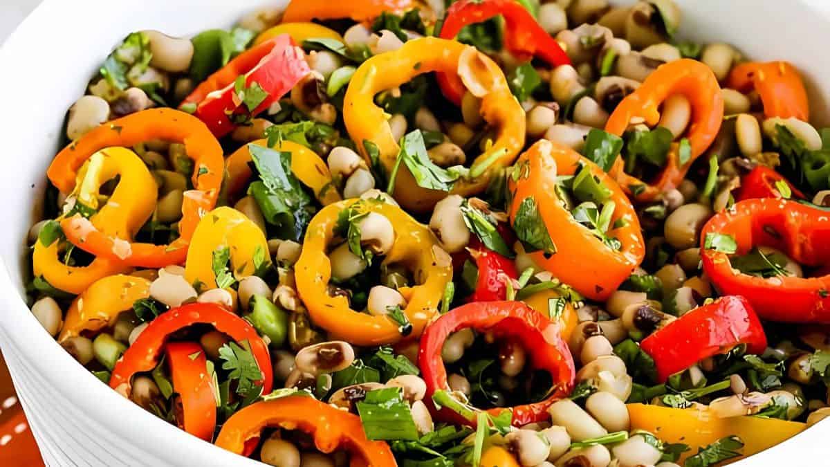 A vibrant salad featuring black-eyed peas, colorful sliced bell peppers, and fresh cilantro, all mixed in a white bowl. The peppers are red, yellow, and orange, adding a pop of color to the dish.