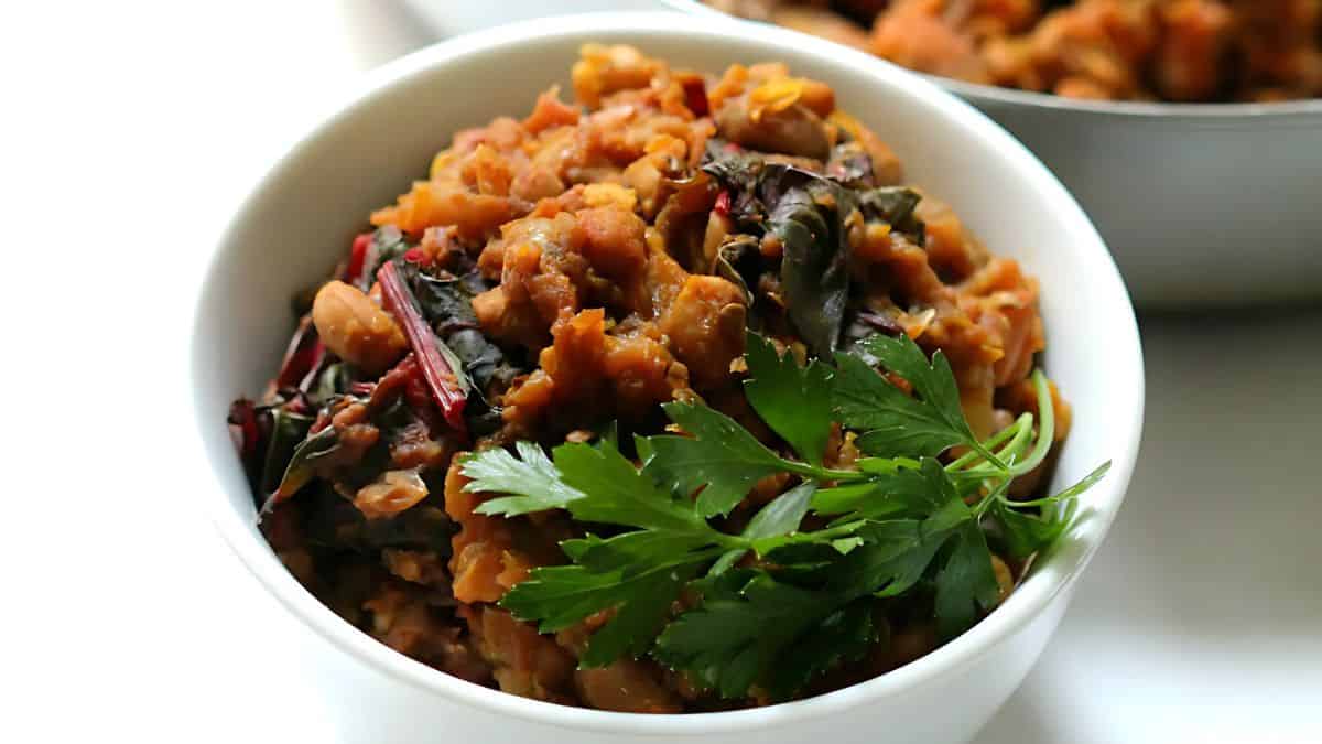 A bowl of spicy vegetarian chili is garnished with fresh parsley. The chili contains beans, greens, and a rich tomato base, creating a hearty and vibrant dish.