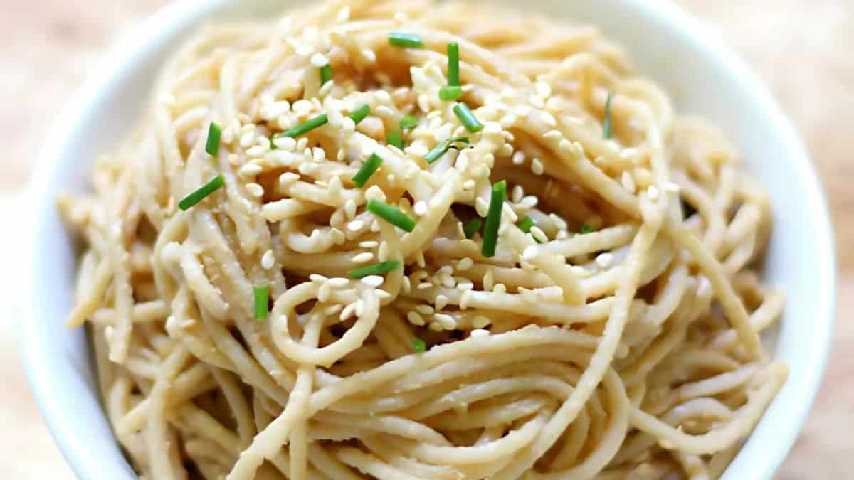 A bowl of cooked noodles topped with sesame seeds and chopped green onions. The noodles appear lightly seasoned and are neatly arranged in the bowl.