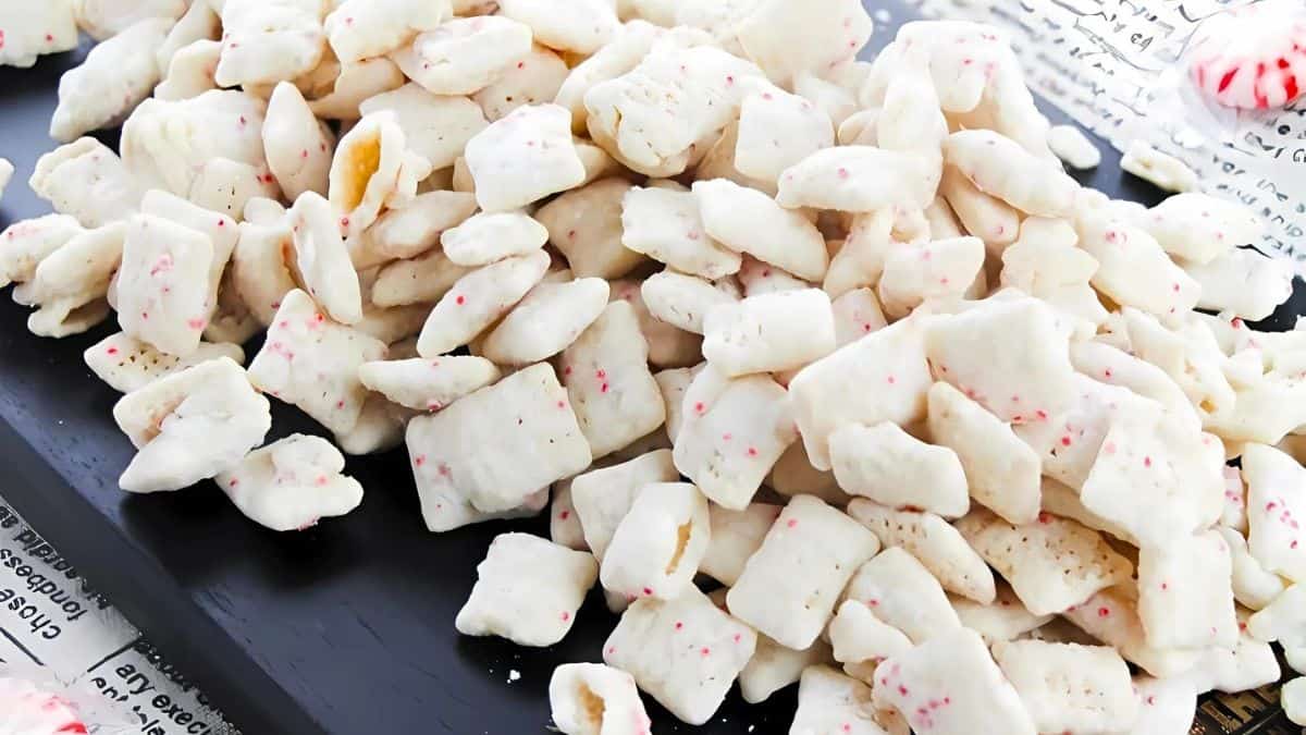 A pile of white, frosted animal crackers with small colored specks displayed on a dark surface. A partially visible newspaper and another cracker are in the background.