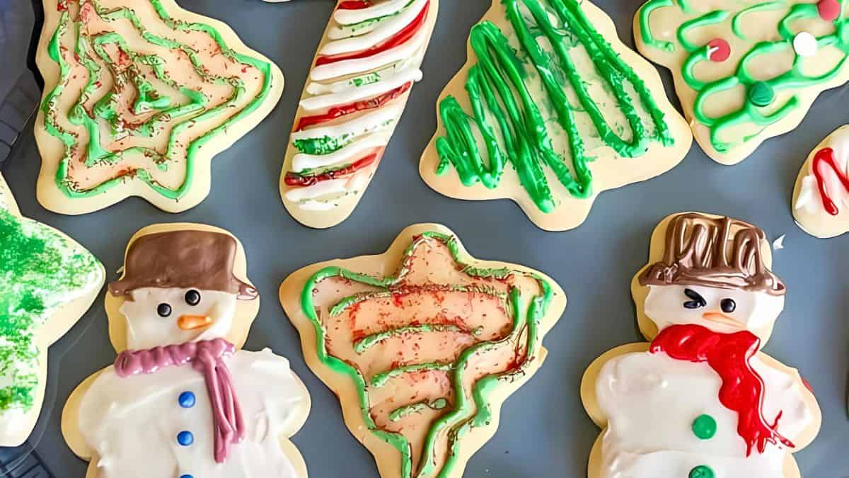 Decorated holiday cookies shaped like snowmen and trees with colorful icing, including green, red, and white patterns and sprinkles, arranged on a tray.