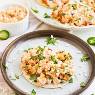 A plate of Street Corn Chicken Tacos topped with a creamy corn, cheese, and herb mixture sits in the foreground.