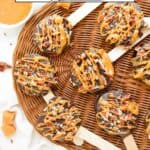 Chocolate-covered apple slices on sticks are arranged on a wicker tray, drizzled with caramel and sprinkled with chopped pecans. A small bowl of caramel sauce and caramel pieces are nearby. Text reads "Chocolate Turtle Apple Slices.