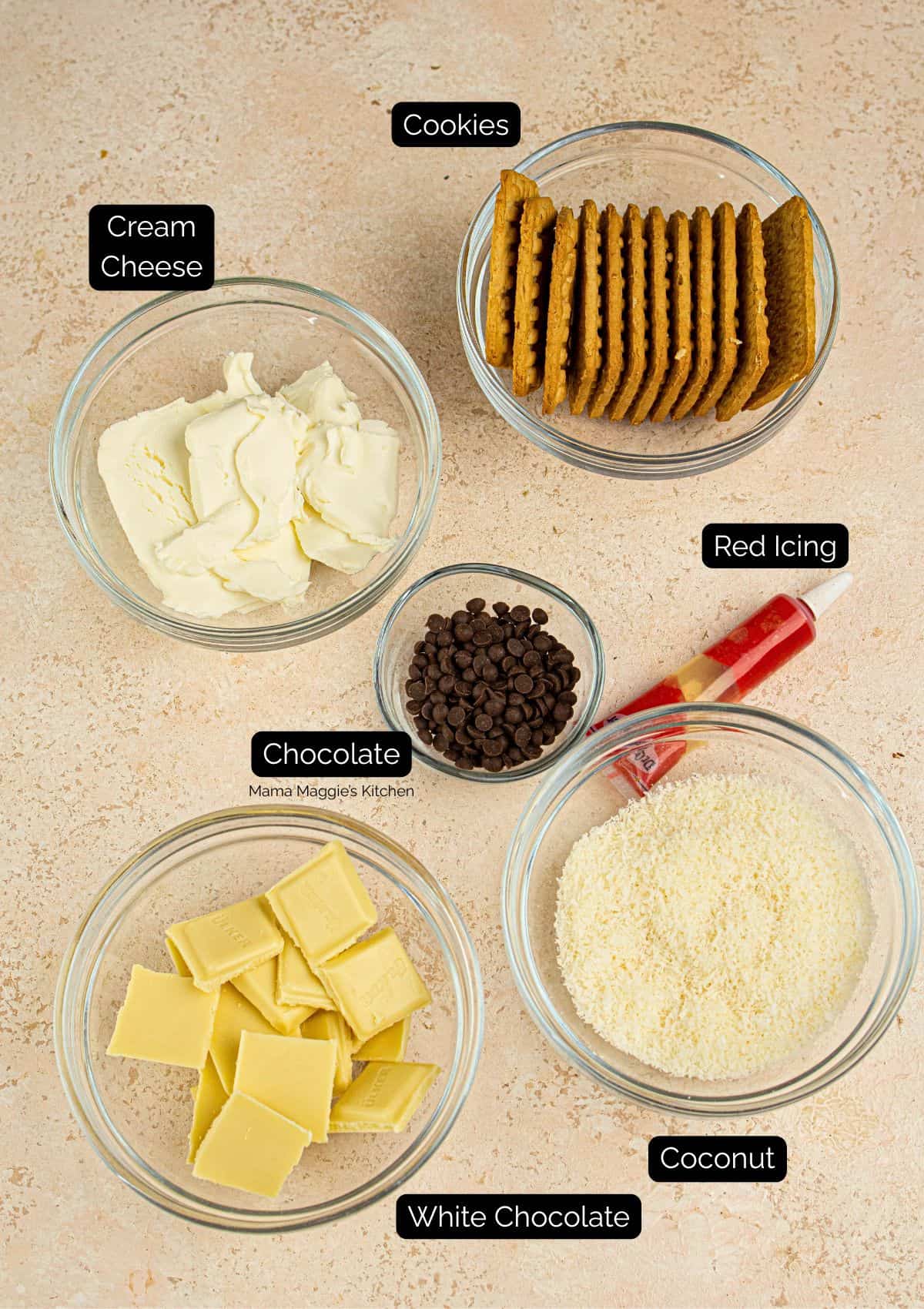 Five labeled bowls and items arranged on a light surface: cookies, cream cheese, chocolate chips, grated coconut, white chocolate squares, and a tube of red icing.