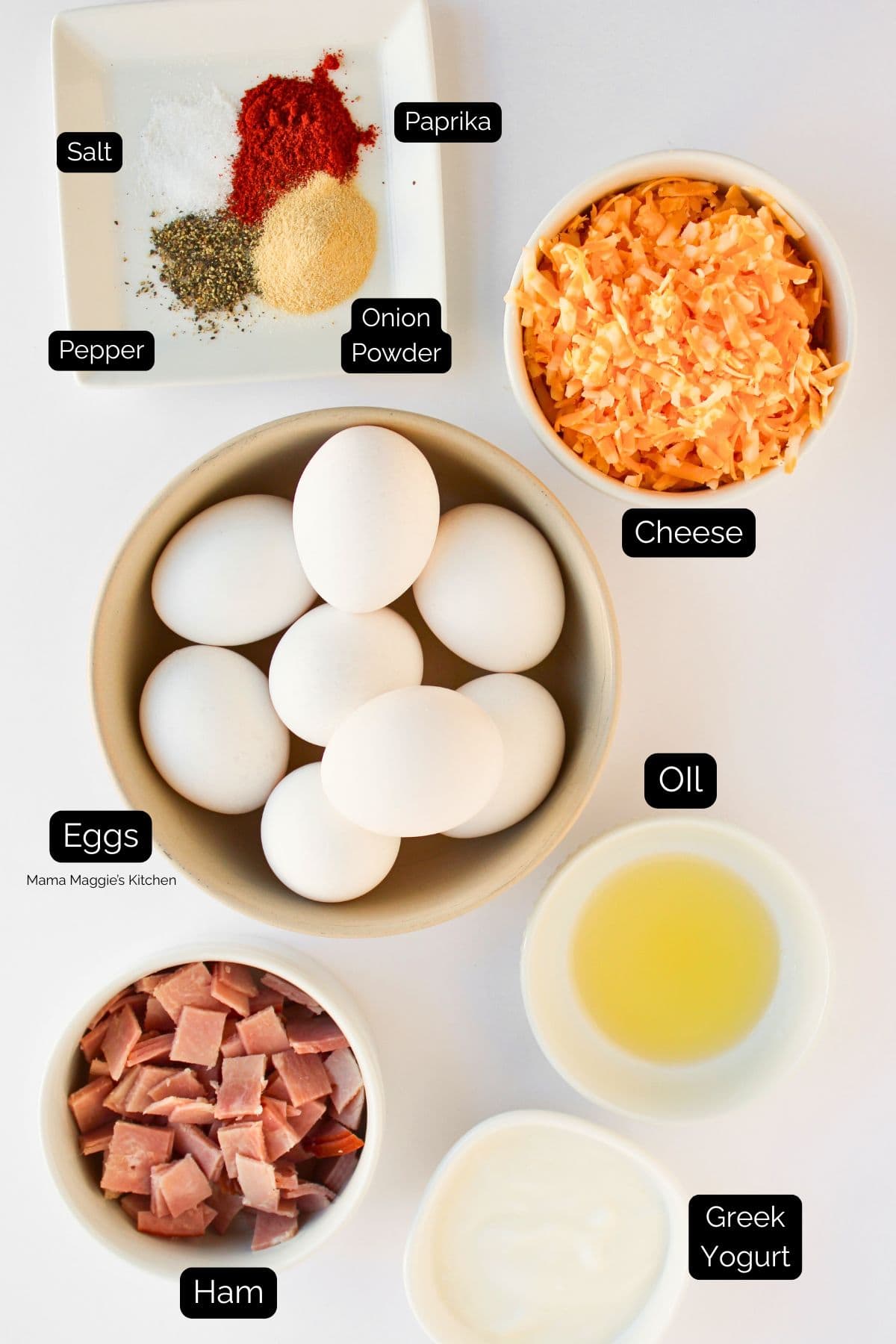 Bowls containing eggs, diced ham, shredded cheese, oil, Greek yogurt, and a plate with spices including salt, pepper, onion powder, and paprika are labeled and arranged on a white surface.