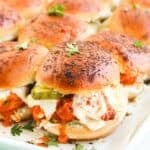 A tray of Buffalo Chicken Sliders with browned buns, melted cheese, chicken in tomato sauce, and pickle slices, garnished with fresh parsley.