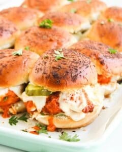 A tray of Buffalo Chicken Sliders with browned buns, melted cheese, chicken in tomato sauce, and pickle slices, garnished with fresh parsley.